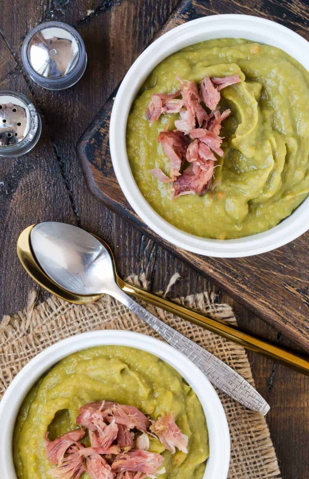 Two bowls of Slow Cooker Split Pea Soup with Ham and two spoons, with shredded ham.