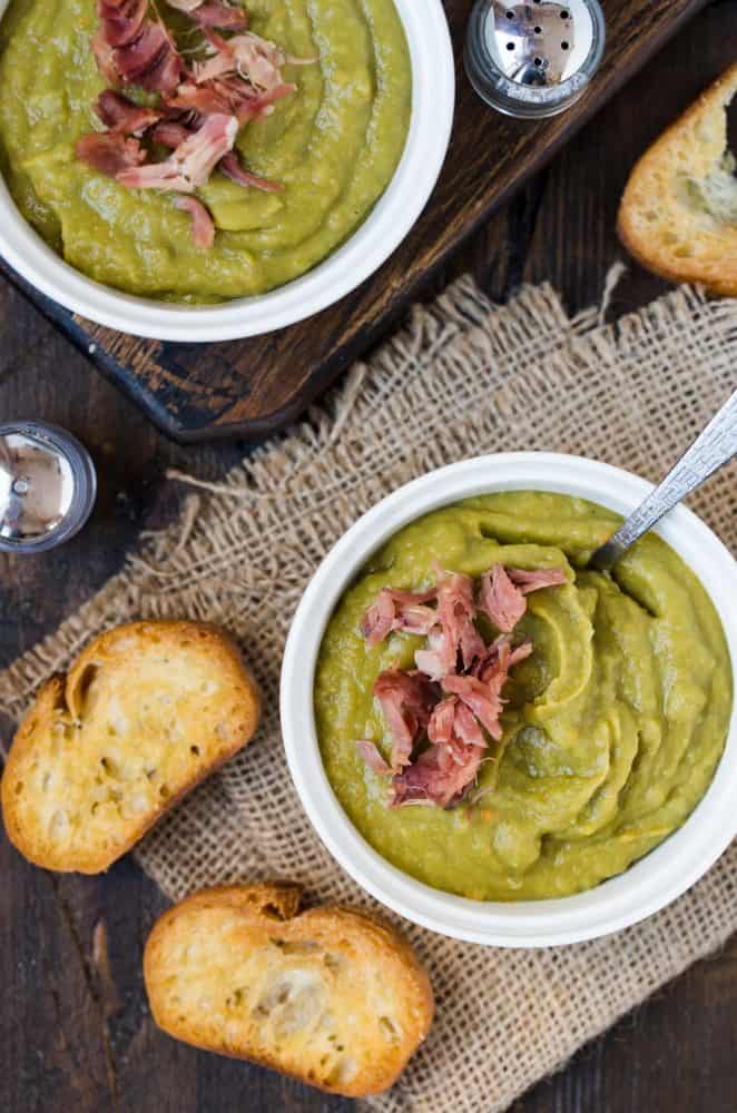 Two bowls of Slow Cooker Split Pea Soup with Ham. Surrounded by toasted crostini pieces and salt and pepper shakers. 