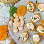 Stuffed Apricots with Goat Cheese, Basil and Marcona Almonds on a gray plate with fresh basil leaves and almonds for garnish.