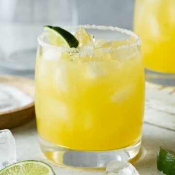 Mango margarita in an ice filled glass rimmed with salt and garnished with lime wedges.