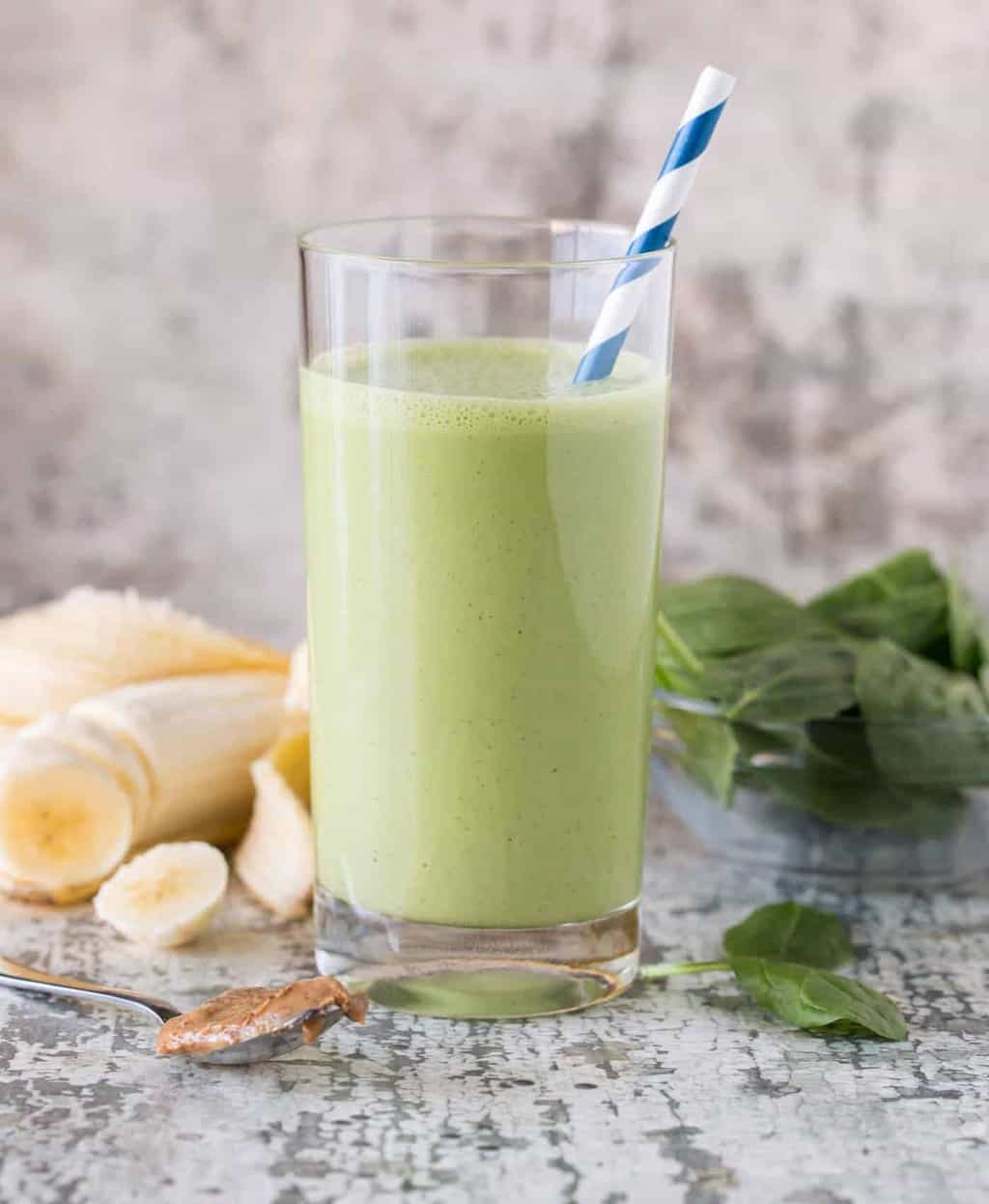 Glass of smoothie on gray countertop with straw. 