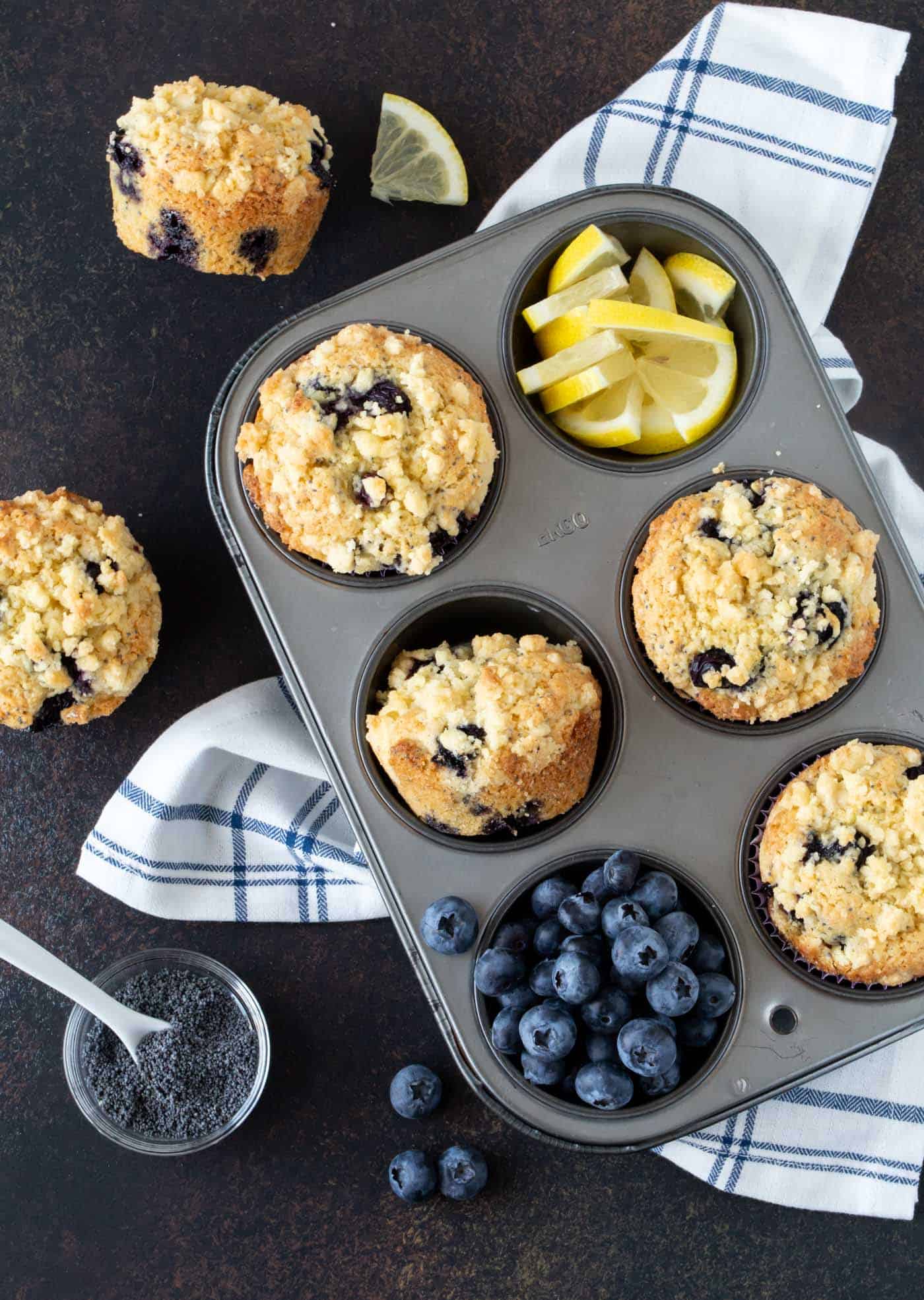 Muffin tin filled with four Blueberry Lemon Poppy Seed Muffins,with fresh blueberries and lemon slices.