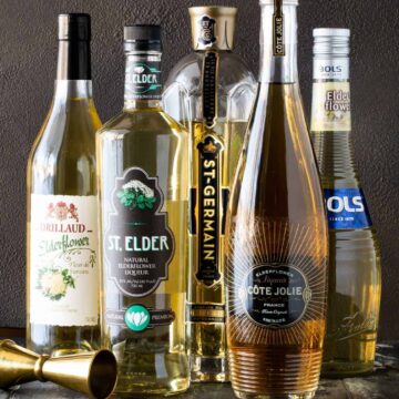 Bottles of different brands of elderflower liqueur with gold jigger.