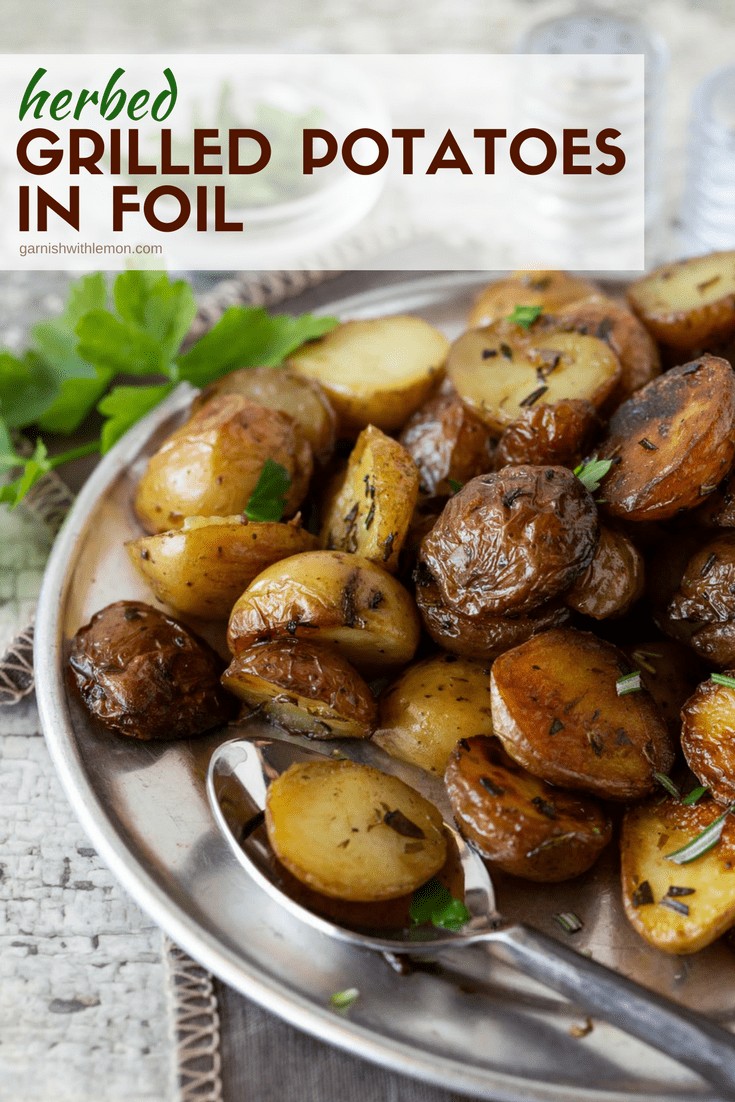 Image of Herbed Grilled Potatoes in Foil on a silver plate with fresh rosemary and fresh parsley. 