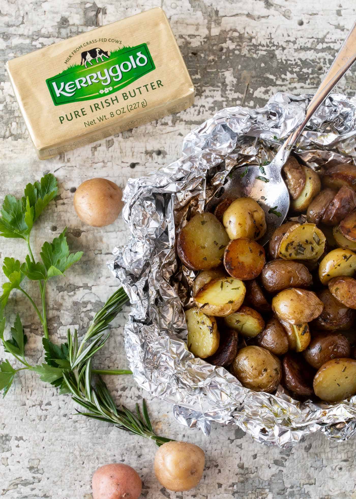 Herbed Grilled Potatoes in Foil packet, garnished with a spoon, fresh rosemary, fresh parsley.