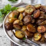 Silver platter full of Herbed Grilled Potatoes in Foil. Garnished with fresh parsley, fresh rosemary, salt and pepper.