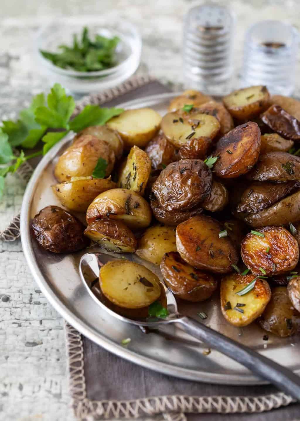 Silver platter full of Herbed Grilled Potatoes in Foil. Garnished with fresh parsley, fresh rosemary, salt and pepper. 