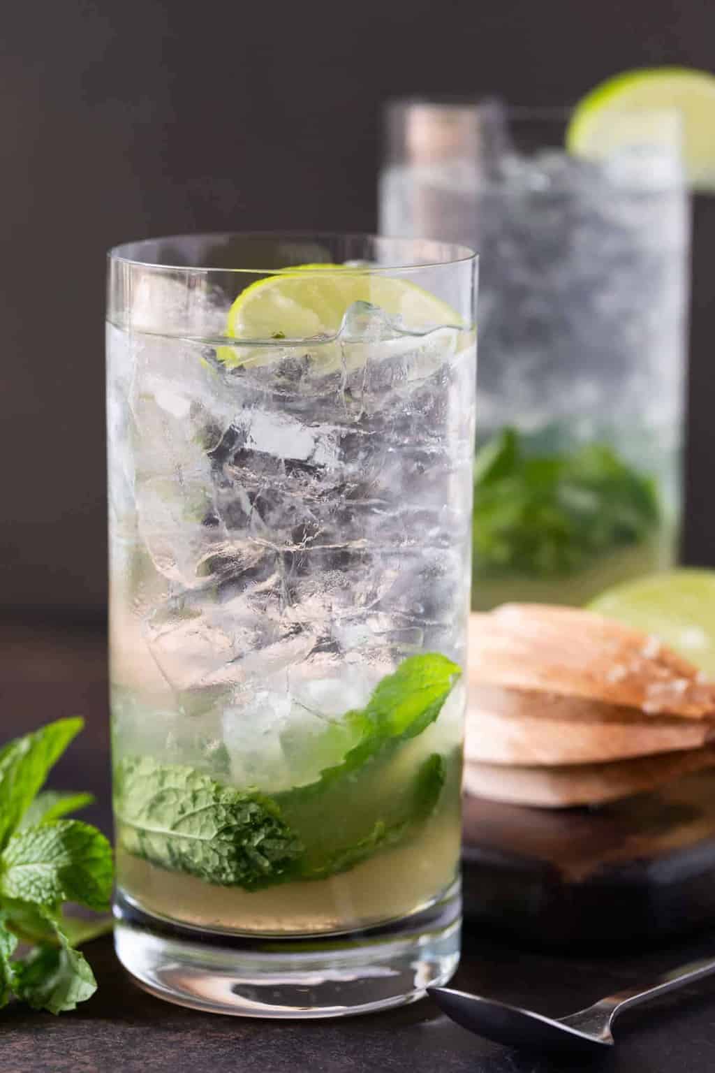 Close up of 2 high ball glasses filled with ice, mint leaves and an elderflower mojito cocktail recipe.
