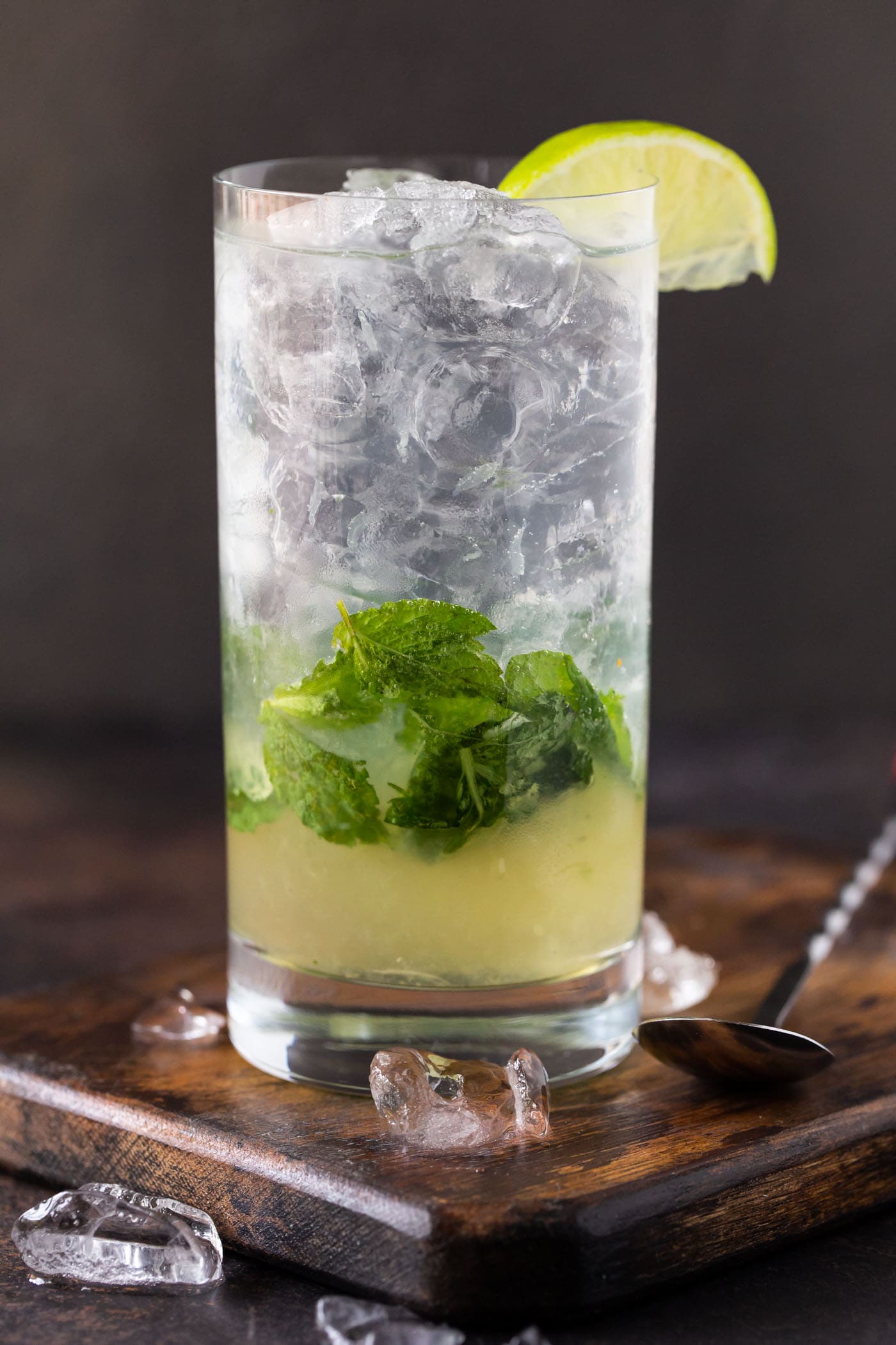 Single high ball glass filled with ice, mint leaves and an elderflower mojito cocktail recipe.