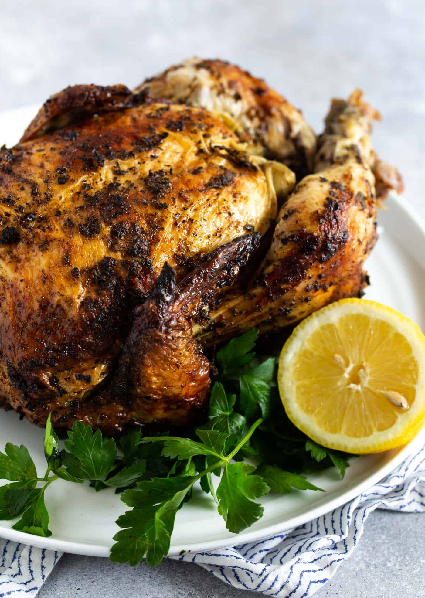 Whole roasted chicken on a white plate garnished with parsley and lemon.