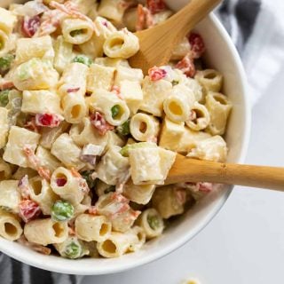 White bowl filled with creamy, Classic Macaroni Salad recipe on a white countertop with two wooden spoons.