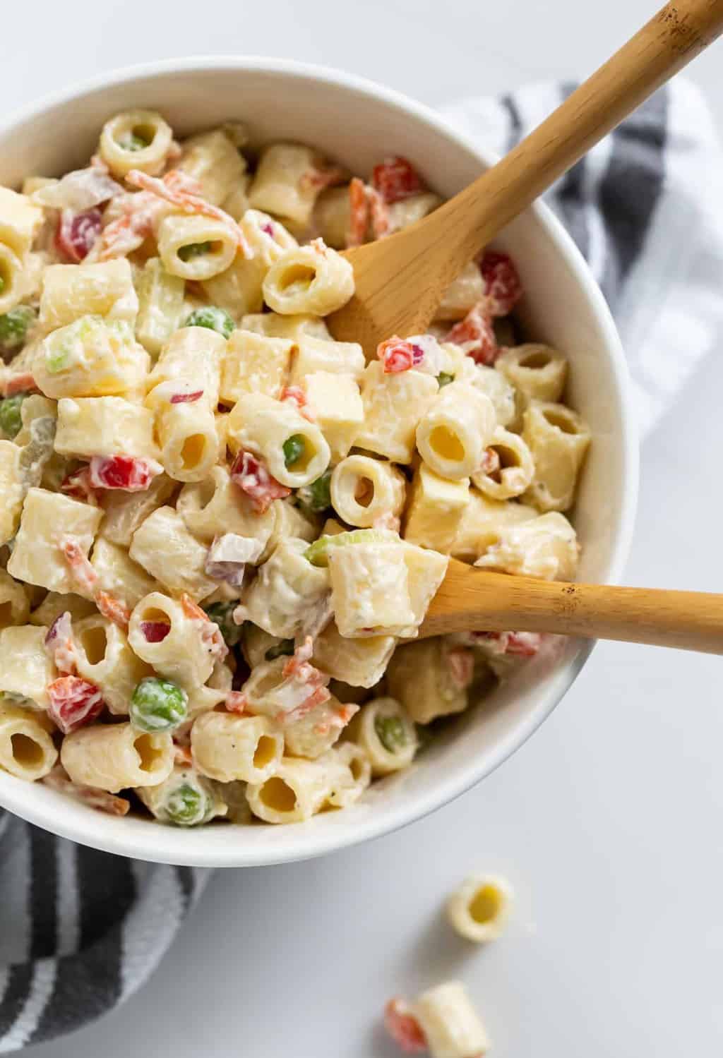 White bowl filled with creamy, Classic Macaroni Salad recipe on a white countertop with two wooden spoons.
