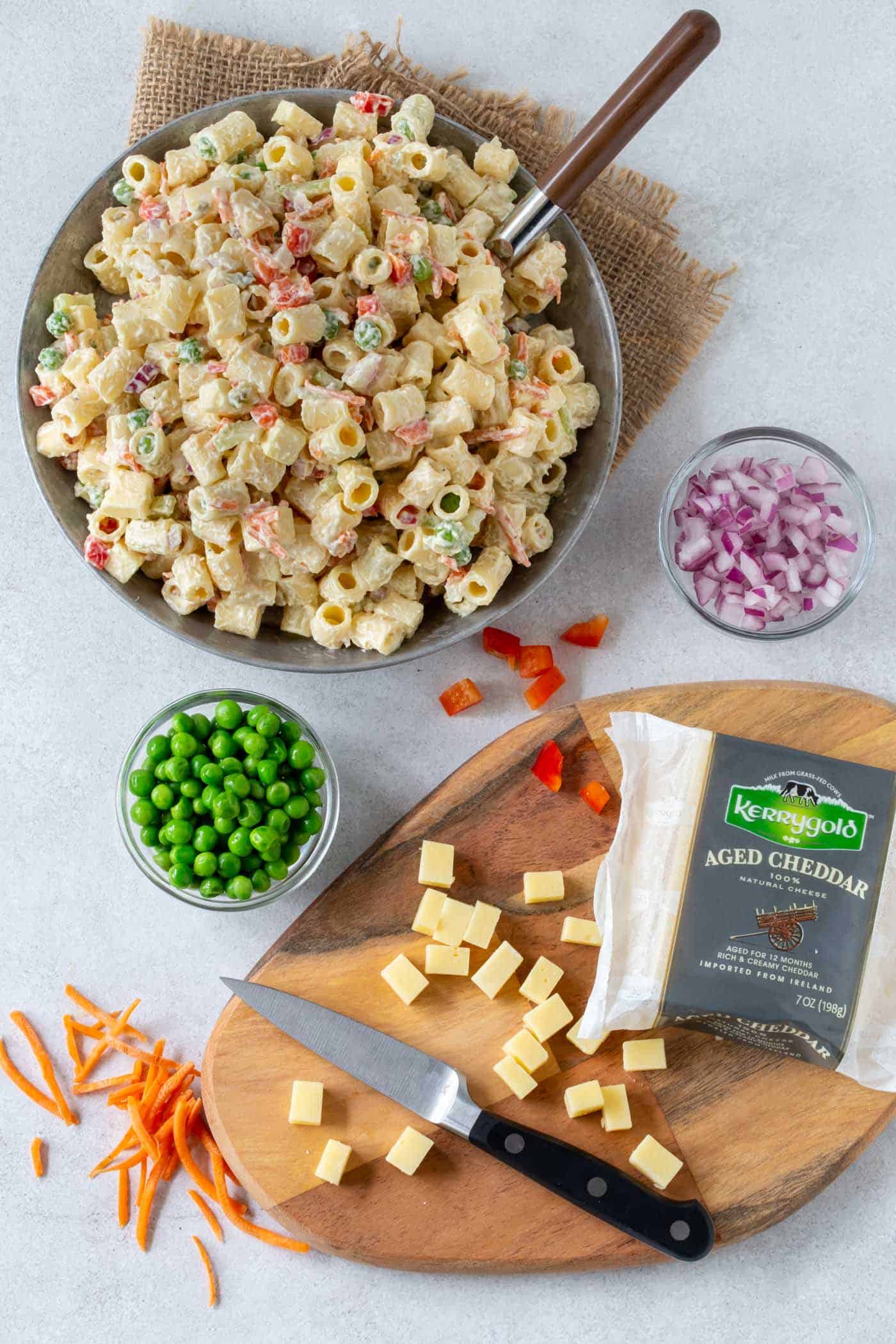 Grey bowl filled with creamy, Classic Macaroni Salad recipe with chopped red onion, bell pepper, carrots and diced Cheddar Cheese.