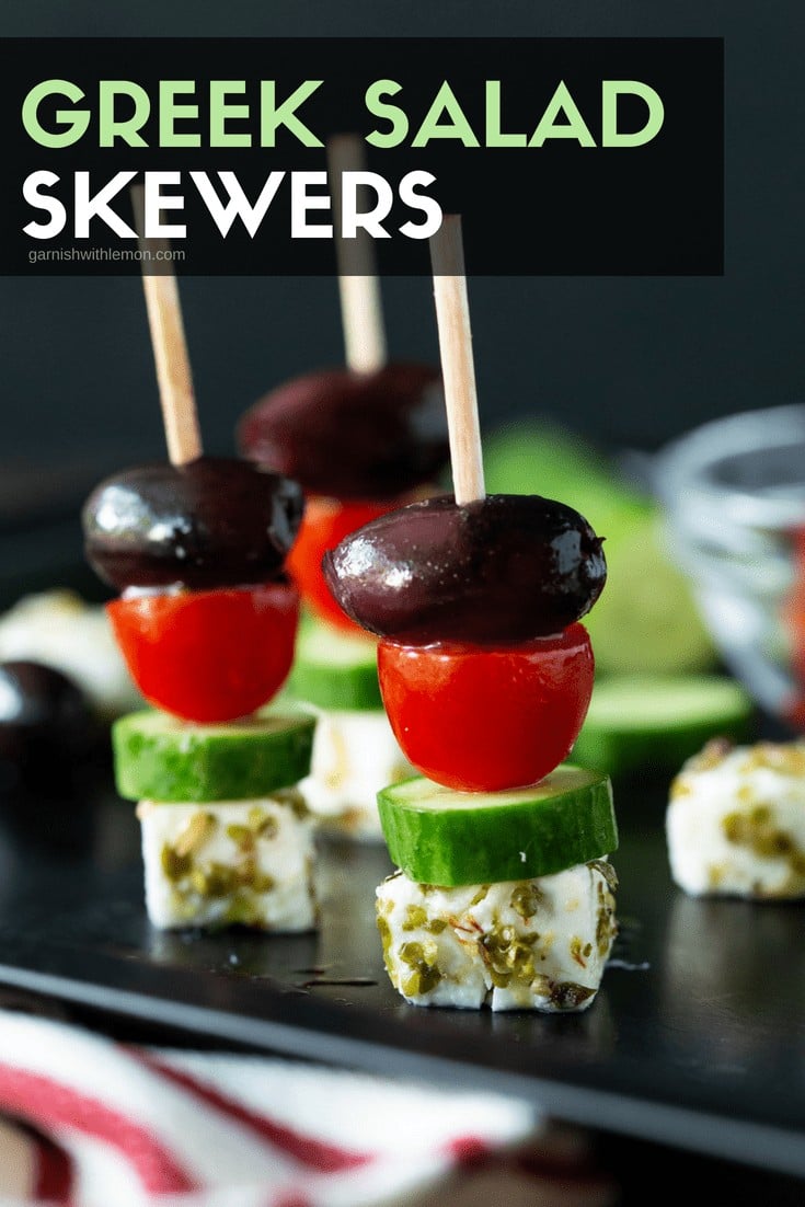 three Greek Salad Skewers made with marinated feta cheese, cucumber, tomatoes and kalamata olives.