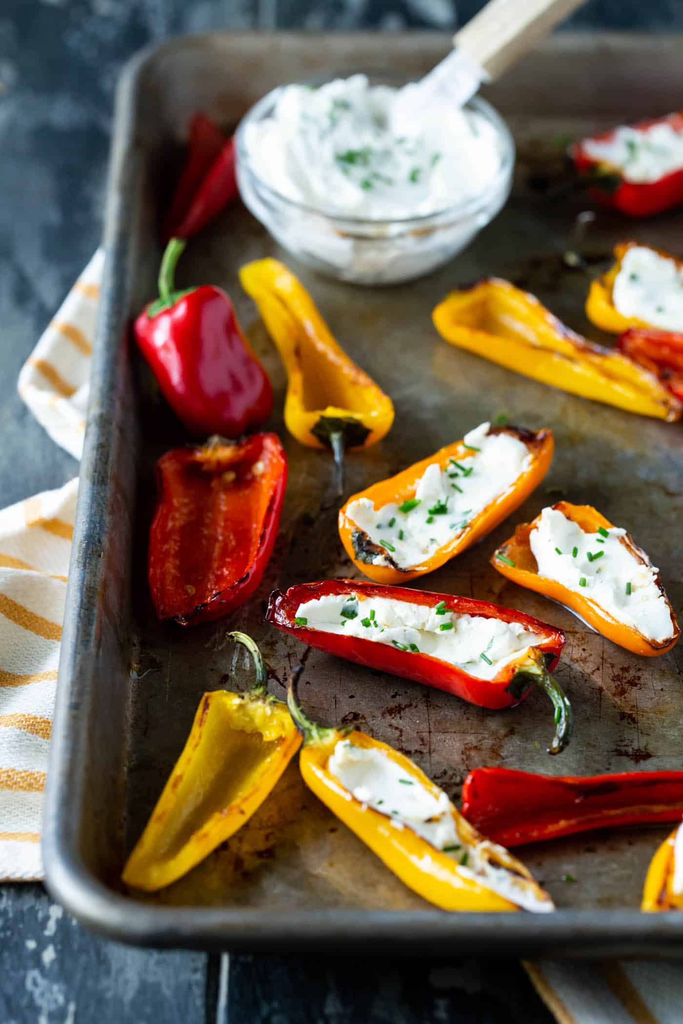 grilled peppers with goat cheese on sheet pan with fresh herbs for garnish and bowl of goat cheese spread on side.