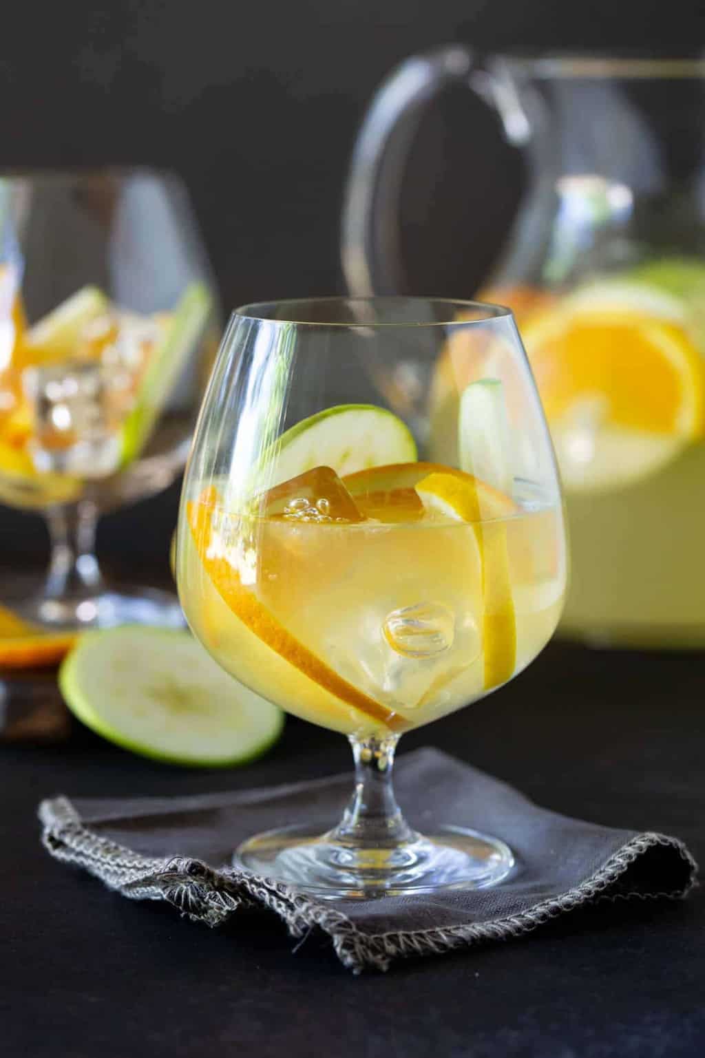 Close up shot of glass of Sangria Lemonade garnished with fresh apples, orange and lemon slices.