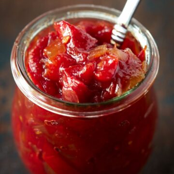 Glass jar filled with tomato jam and a spoon.