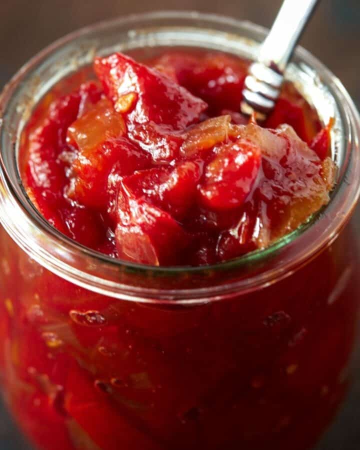 Glass jar filled with tomato jam and a spoon.
