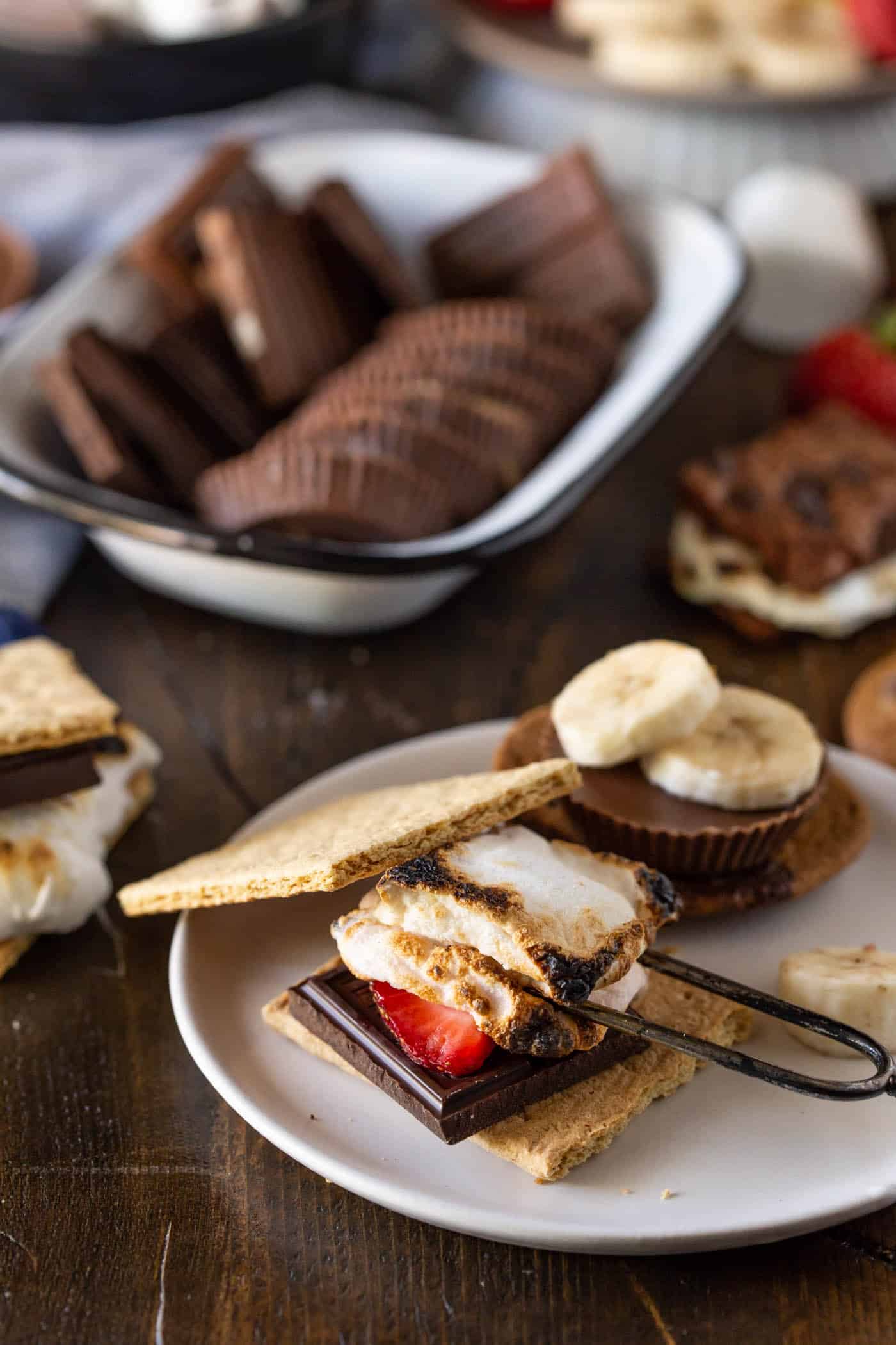 Roasted marshmallow on top of dark chocolate with strawberry slice on a graham cracker.