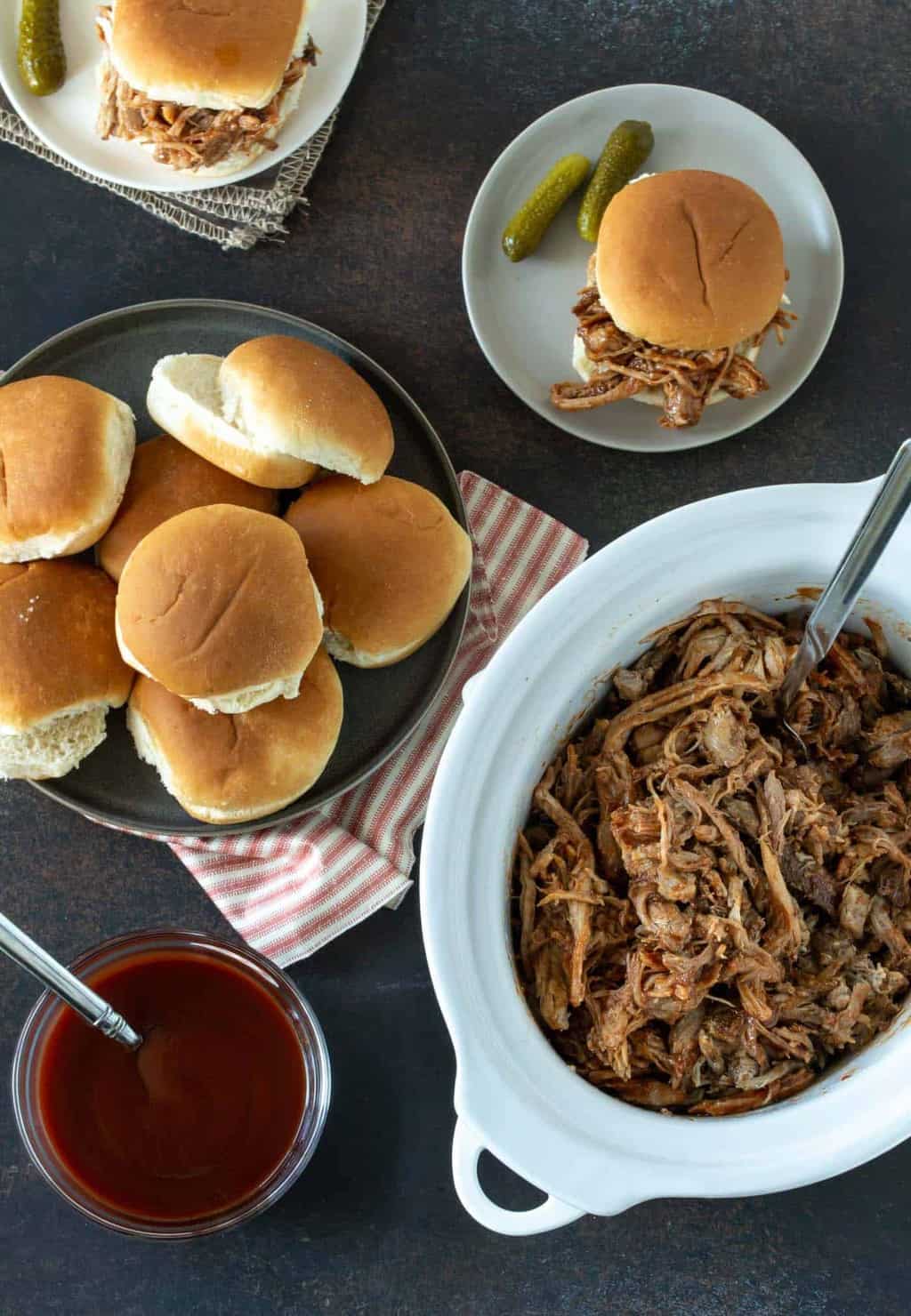 pulled pork in white slow cooker with buns on side for serving.