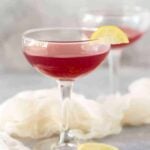 Two coupe glasses filled with Pomegranate Gin Cocktails on a grey board and garnished with small lemon slices.