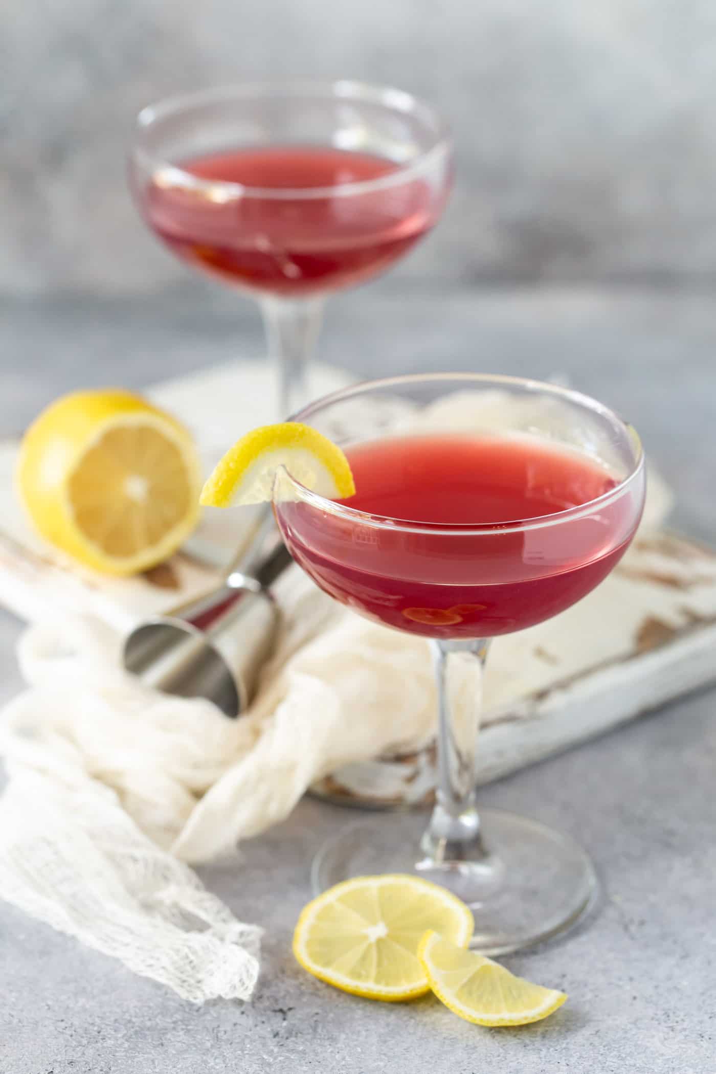 Two coupe glasses filled with Pomegranate Gin Cocktails. Set on a white board with lemon slice garnishes.