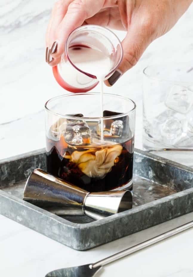 cream being poured into a white russian cocktail.