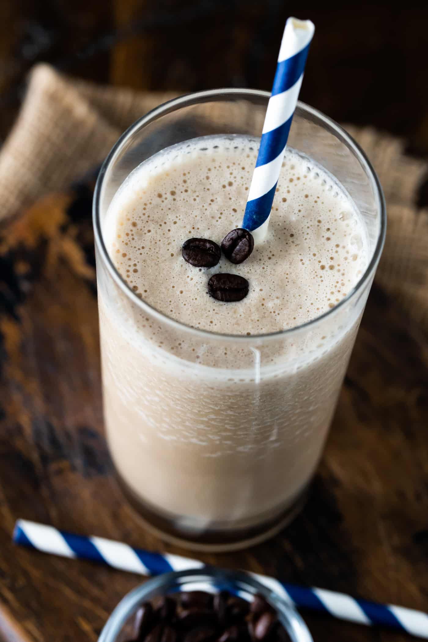 smoothie in a high ball glass on a dark background. Garnished with coffee beans and a straw.