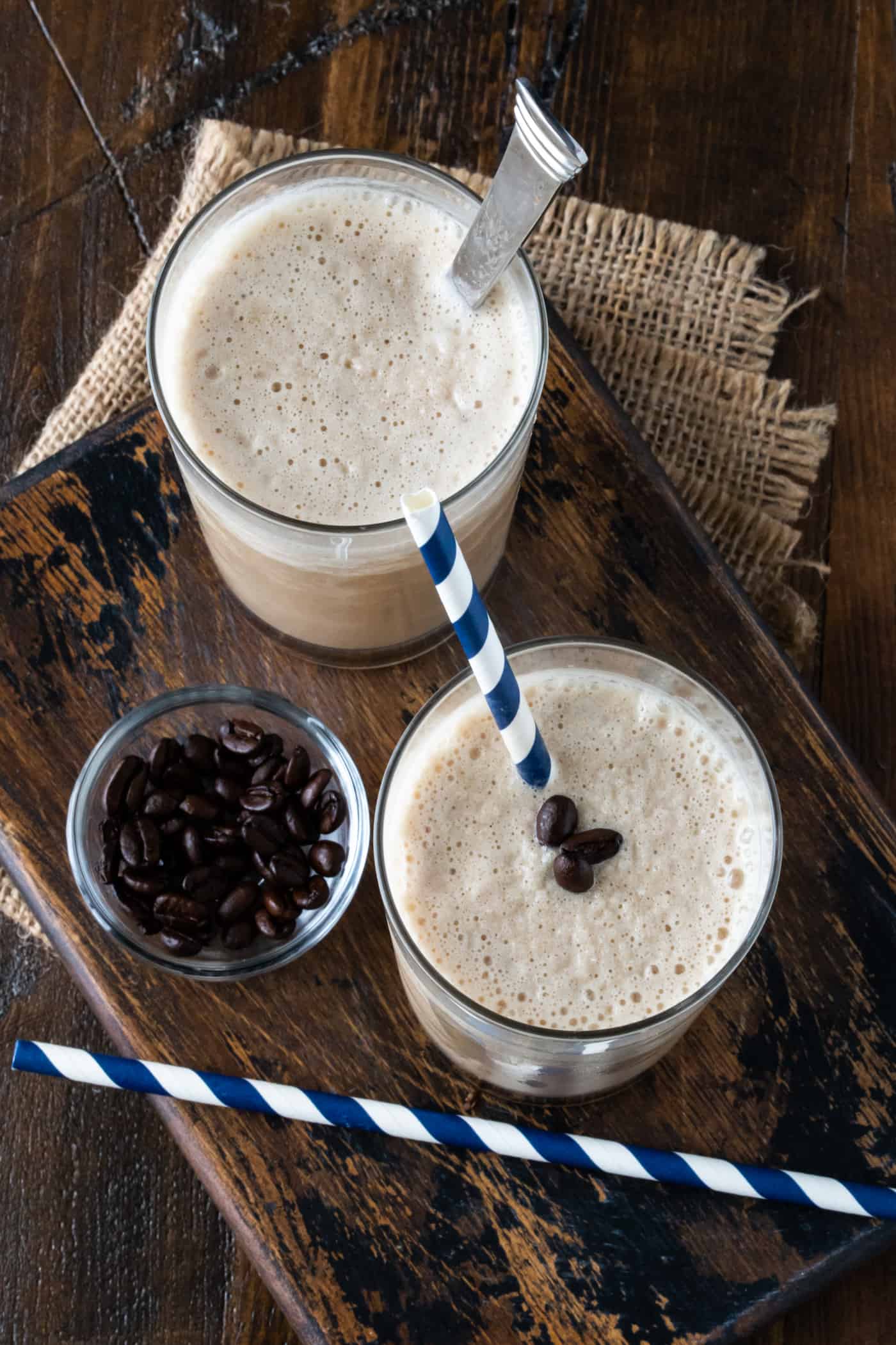  2 coffee smoothies in high ball glasses with a bowl of coffee beans for garnish.