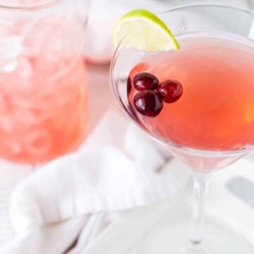 Martini in tall glass on a white background with fresh cranberries and lime wedges for garnish.