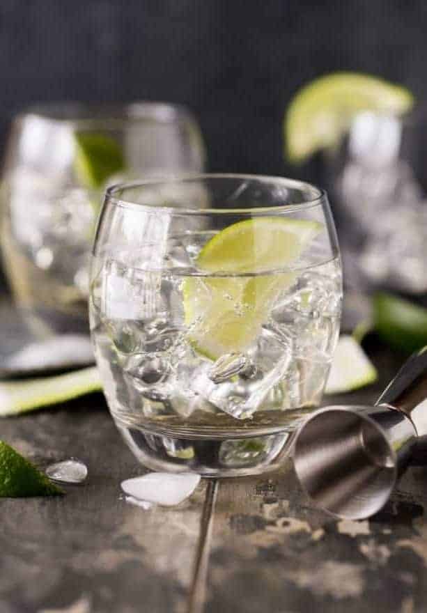 low ball glass with gin and tonic and limes.