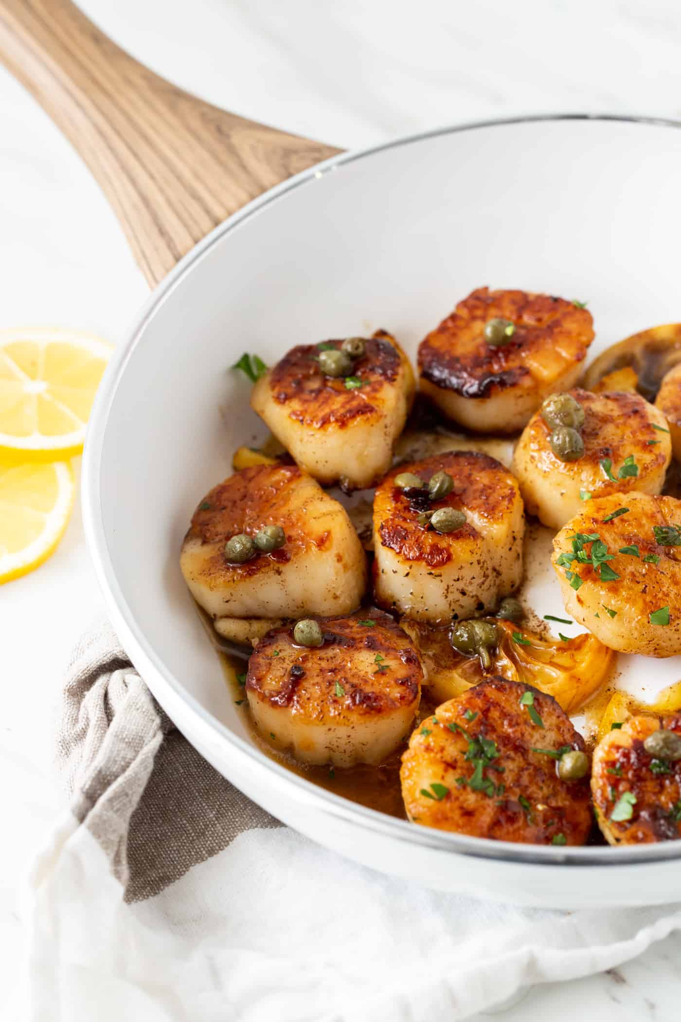 Scallops with Lemon, Capers and Brown Butter in a white bowl with fresh lemon slices for garnish.