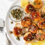 seared scallops in a white bowl with capers and lemon slices for garnish.