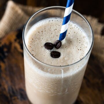 Tall glass of coffee smoothie with blue and white striped straw.