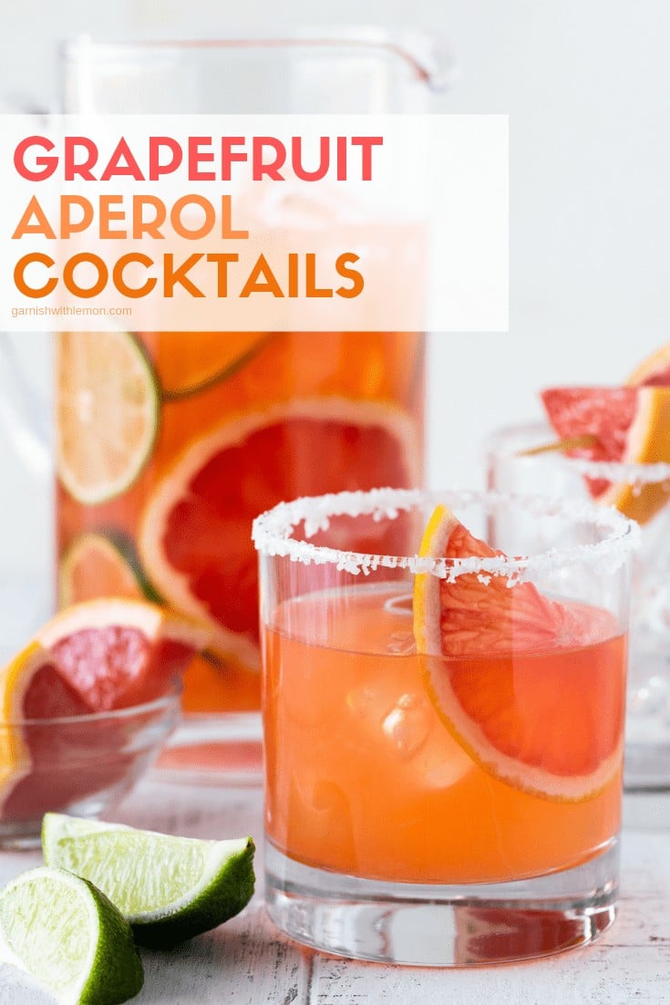 Grapefruit Aperol Cocktails in a pitcher and a low ball glass with a salt rim on a white background.