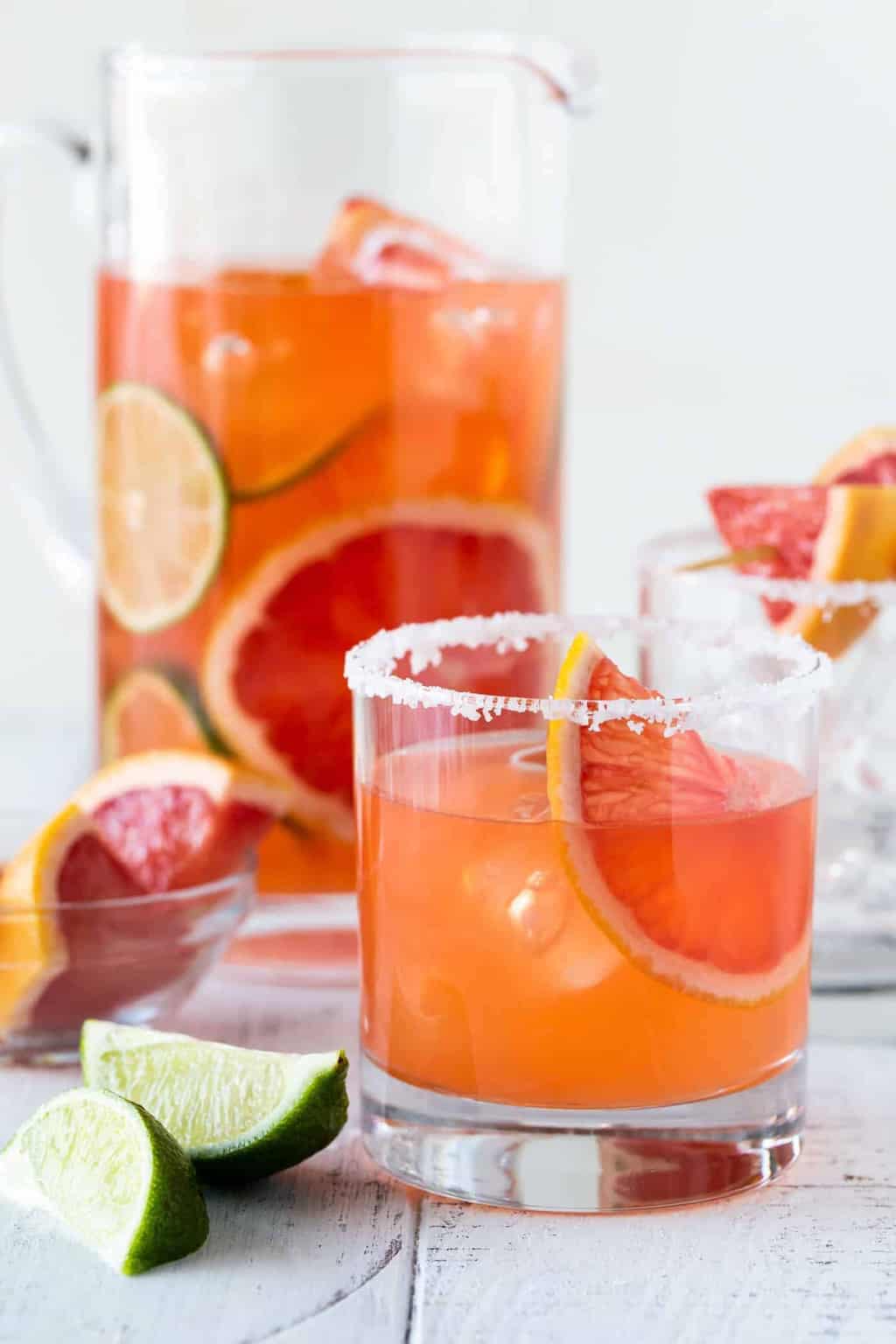 Graperfuit Aperol Cocktails in a low ball glass with a salt rim. Pitcher of Grapefruit Aperol cocktails with fresh grapefruit slices.