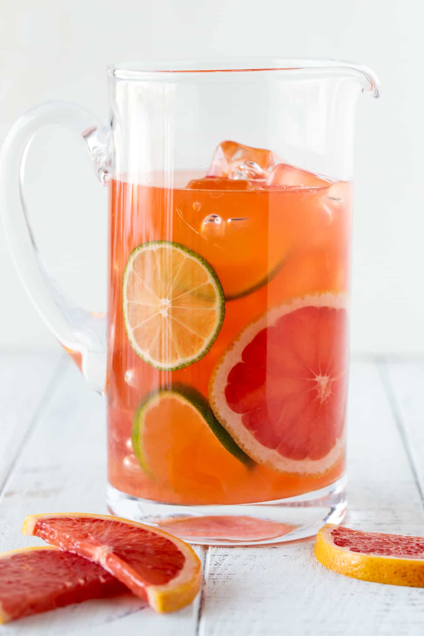 Glass pitcher filled with Grapefruit Aperol Cocktails garnished with fresh grapefruit and limes slices.