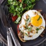 An open-faced Mushroom and Fried Egg Sandwich on a dark gray plate with a side salad.