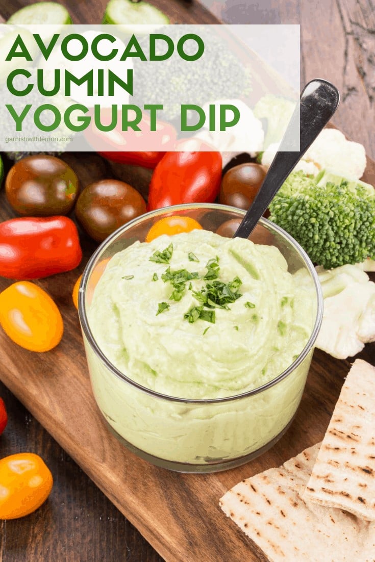 Avocado Cumin Yogurt Dip in a small glass bowl surrounded by fresh cherry tomatoes and broccoli for dipping.