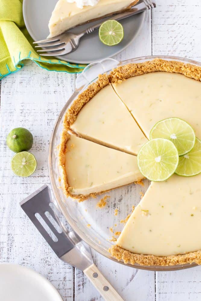  sliced key lime pie in a glass pie plate with fresh lime slices for garnish.