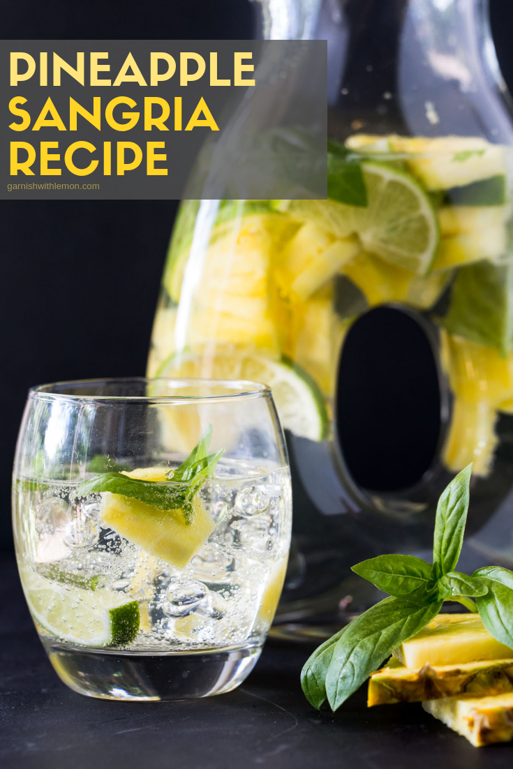 Pitcher of Pineapple Sangria recipe with a glass of sangria garnished with fresh pineapple and basil.