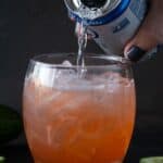 glass filled with orange drink with club soda being poured on top