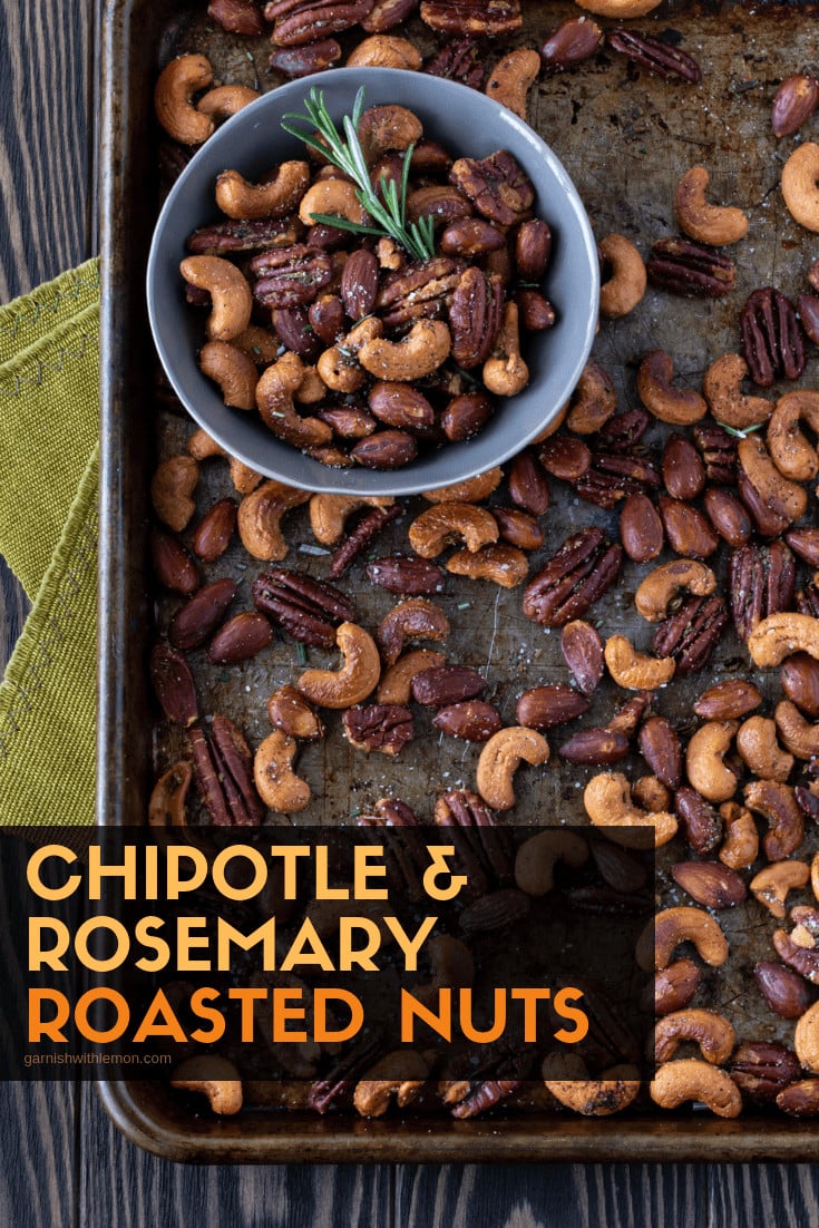 Nuts on s sheet pan with a small bowl of roasted nuts that is garnished with fresh rosemary.