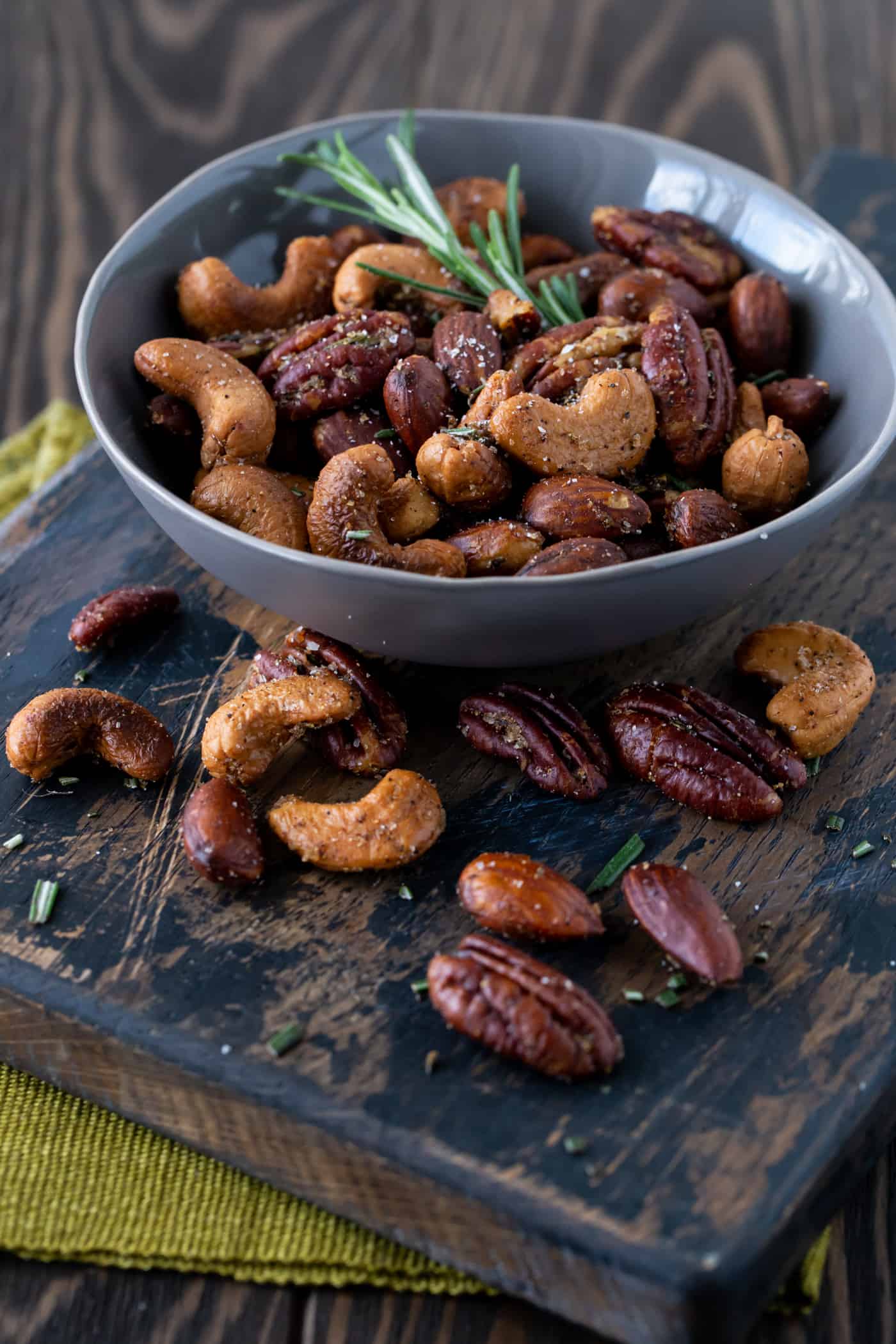 Serving bowl of  Nuts on a dark background with fresh rosemary for garnish.