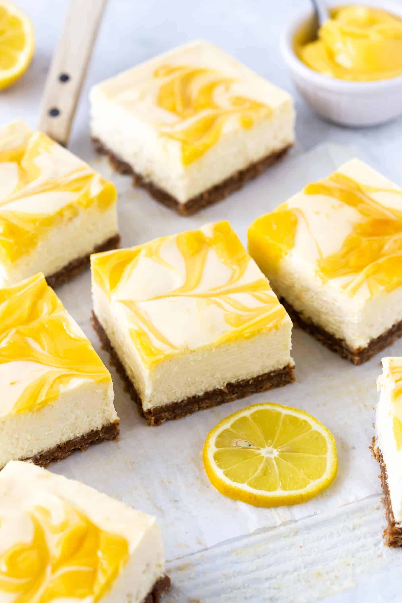 Lemon Cheesecake Bars topped with swirled fresh lemon curd on white parchment paper. 