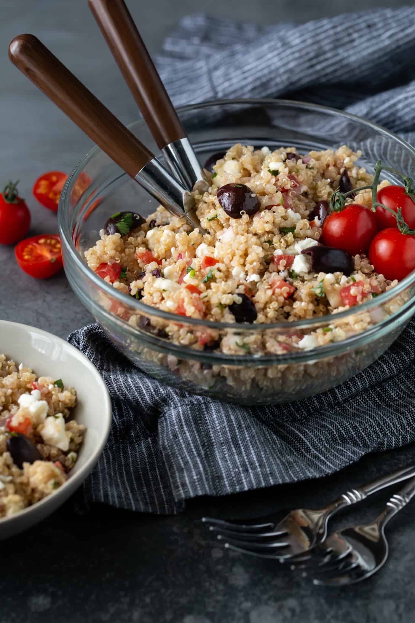 Mediterranean Quinoa Salad in a glass bowl on a dark background garnished with sliced grape tomatoes.