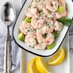 Shrimp Salad with Avocado in a white serving dish with a silver spoon  and fresh lemon wedges.