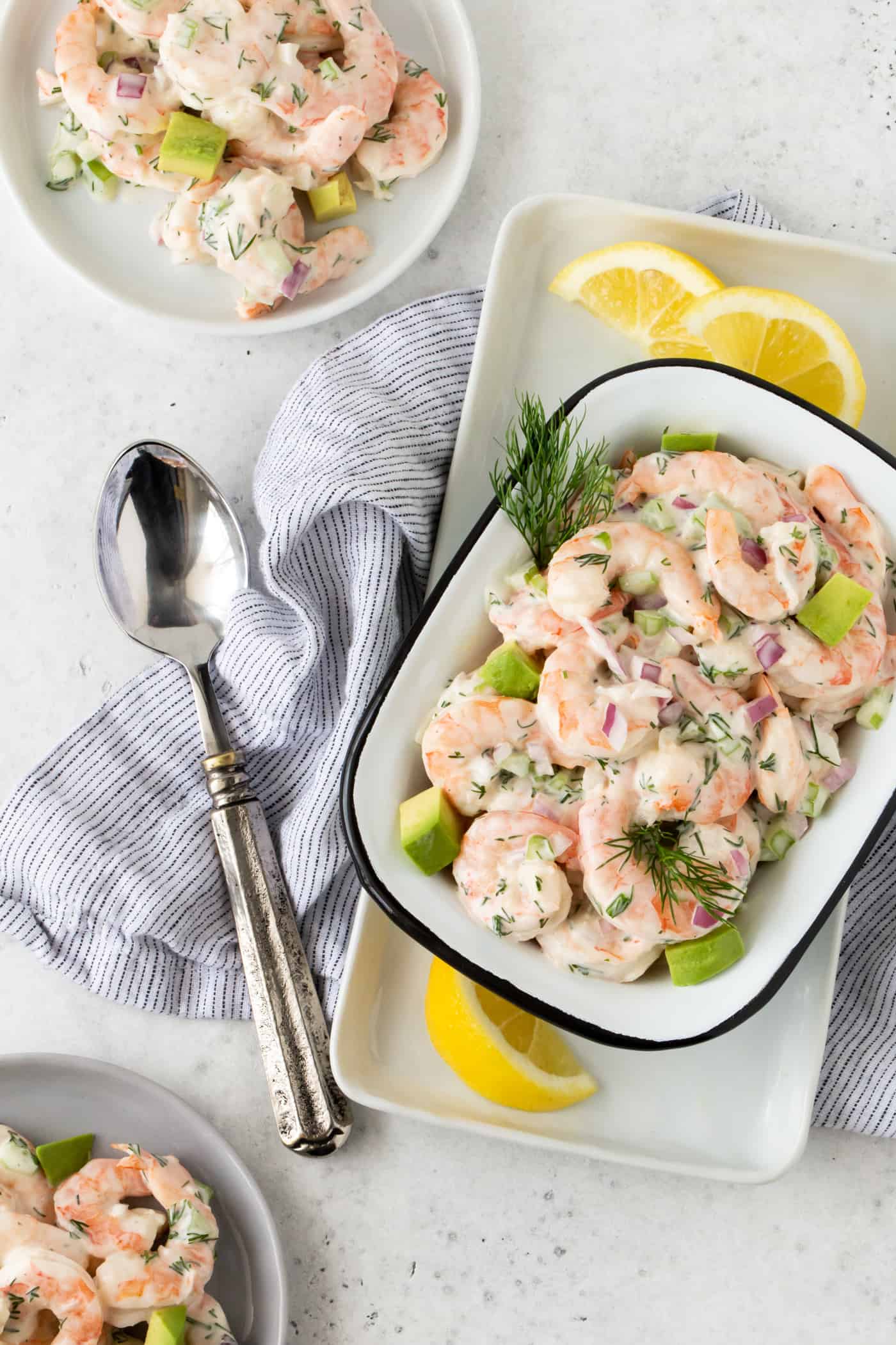 Shrimp Salad with Avocado in a white bowl with fresh dill and lemon wedges on a white surface.