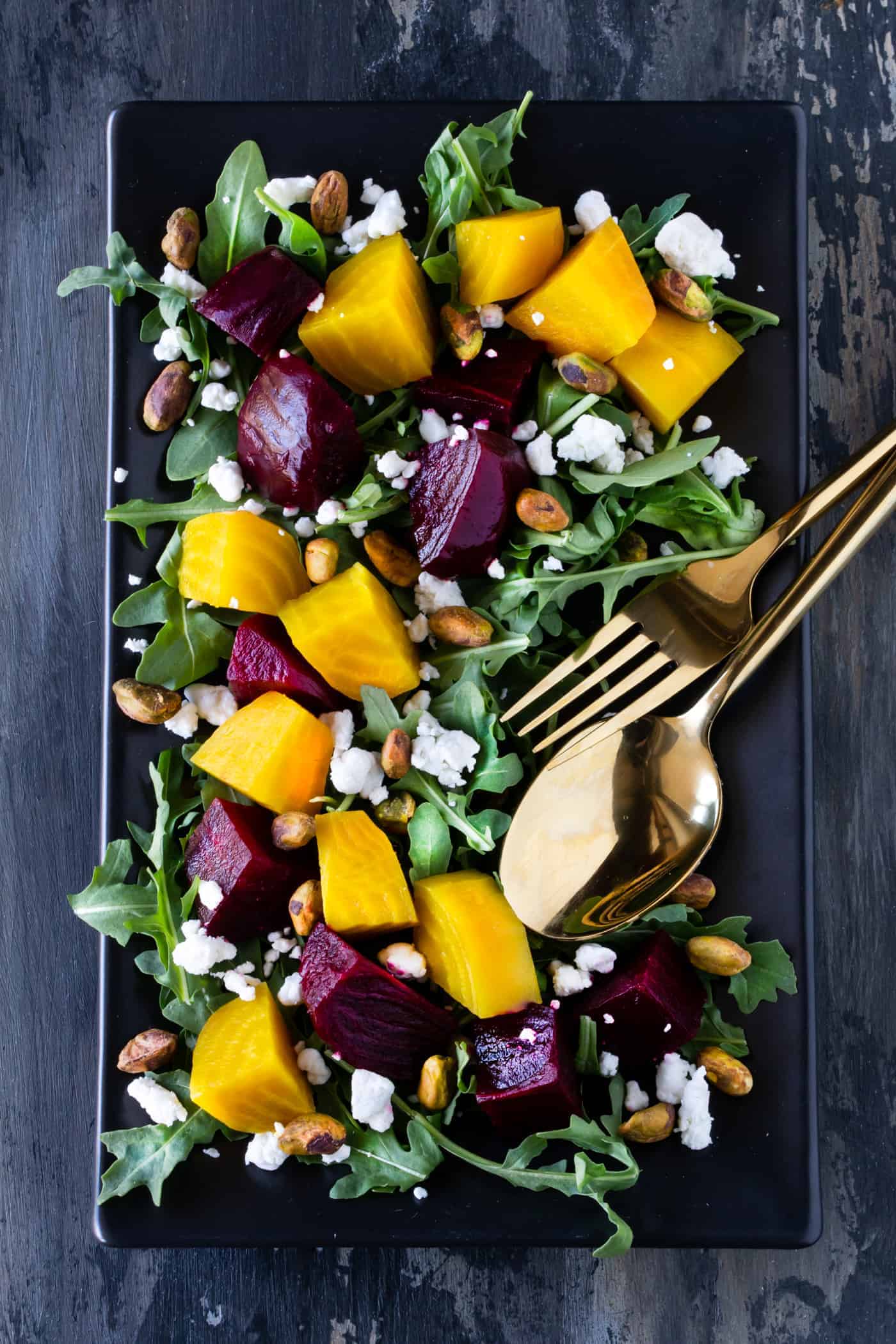 Black platter of Roasted Beet Salad with Goat Cheese, Arugula and Pistachios with a tangy balsamic glaze.