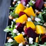 Close up of Roasted Beet Salad with Goat Cheese, Arugula and Pistachios on a black platter.